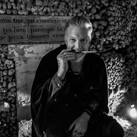 Josh Homme un couteau entre les dents dans les catacombes, devant une épitaphe latine